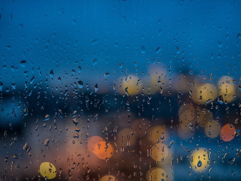 Rain on a window blurring city lights into colorful bokeh at dusk.